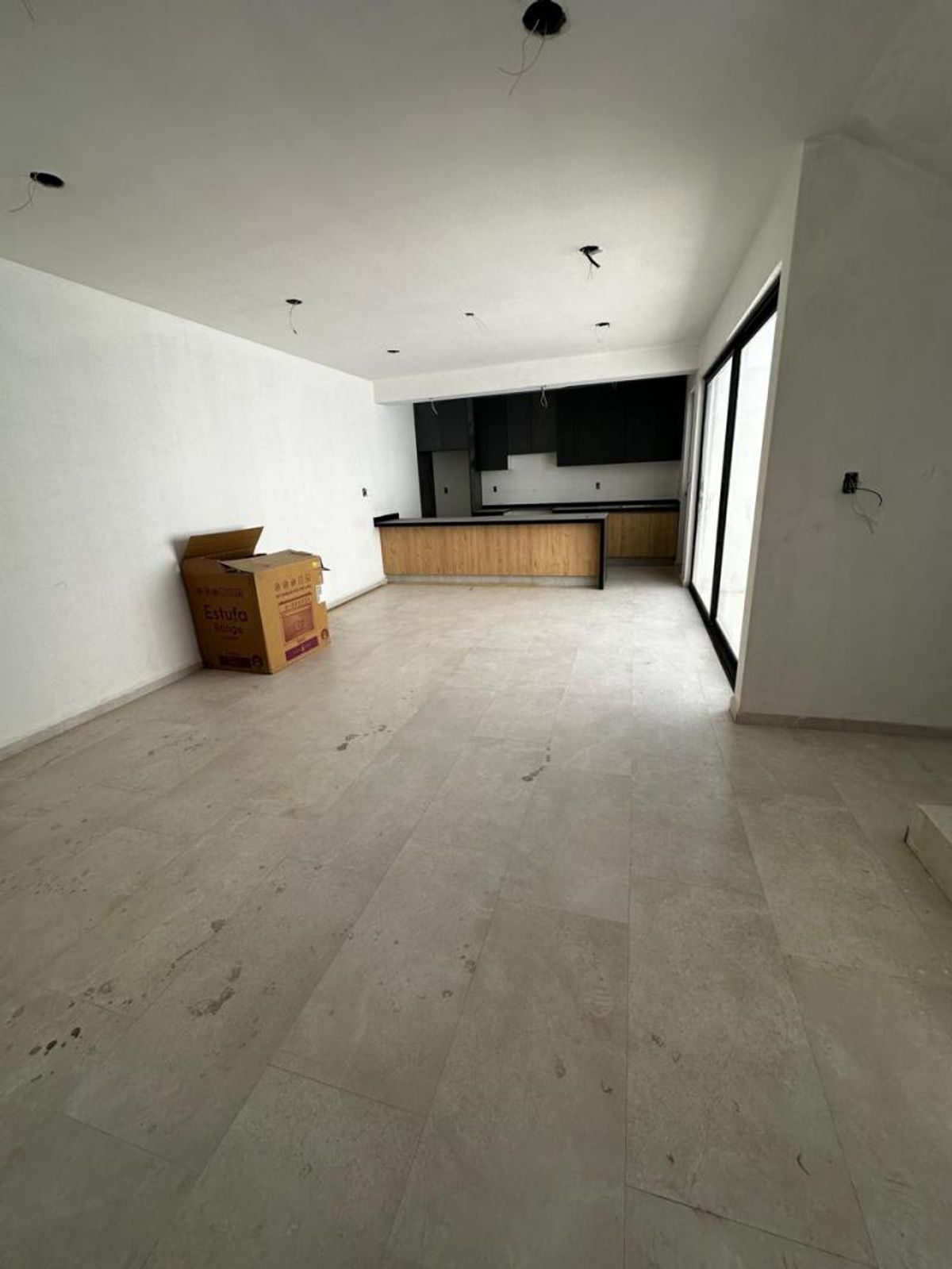 Espacio interior sin amueblar con piso claro, puertas de cristal y cocina al fondo