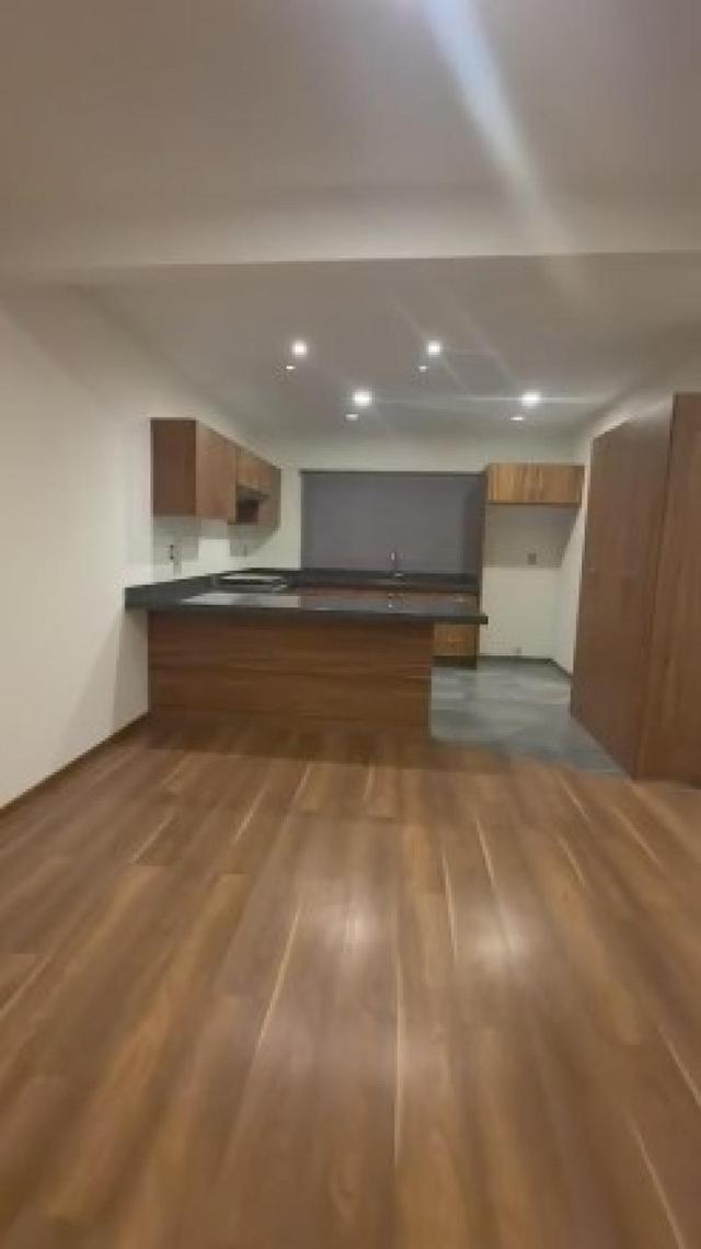 Cocina abierta con barra de madera, cubierta oscura, gabinetes, luces empotradas y piso laminado