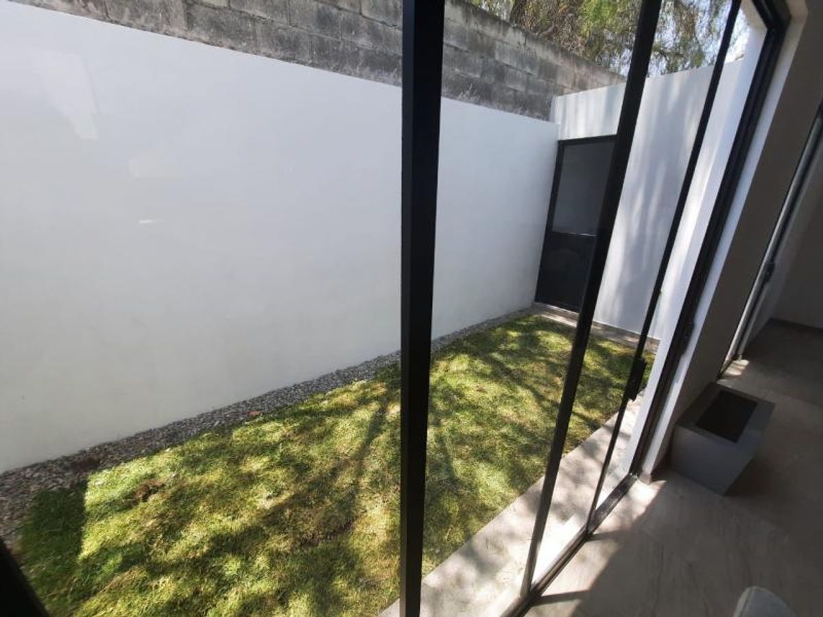 Jardín interior con césped y muro alto blanco visto desde puertas corredizas de cristal
