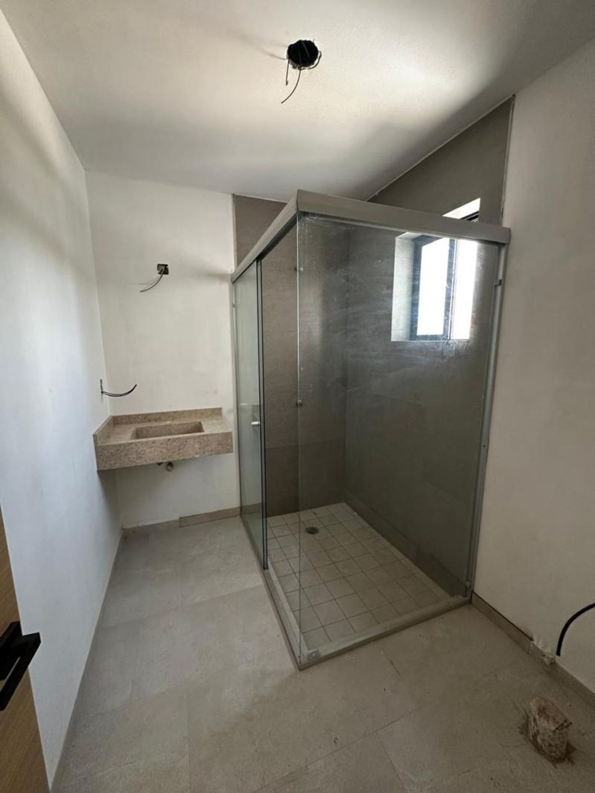 Baño con cancel de cristal en la regadera, lavabo de piedra y piso gris