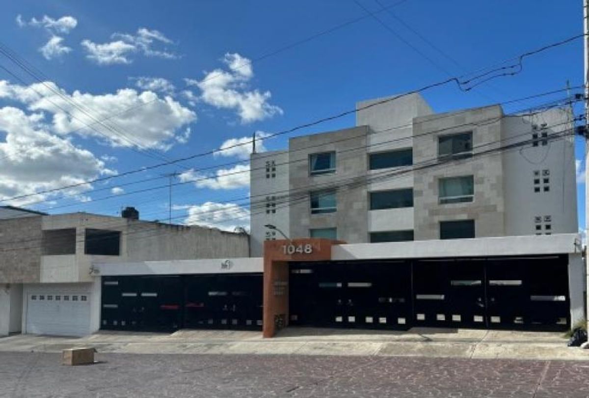 Edificio residencial de fachada clara con piedra, portón negro y número 1048