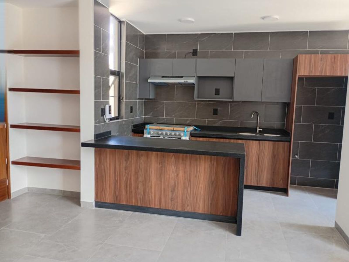 Cocina integral con barra de madera, cubierta negra, gabinetes grises y repisas de madera