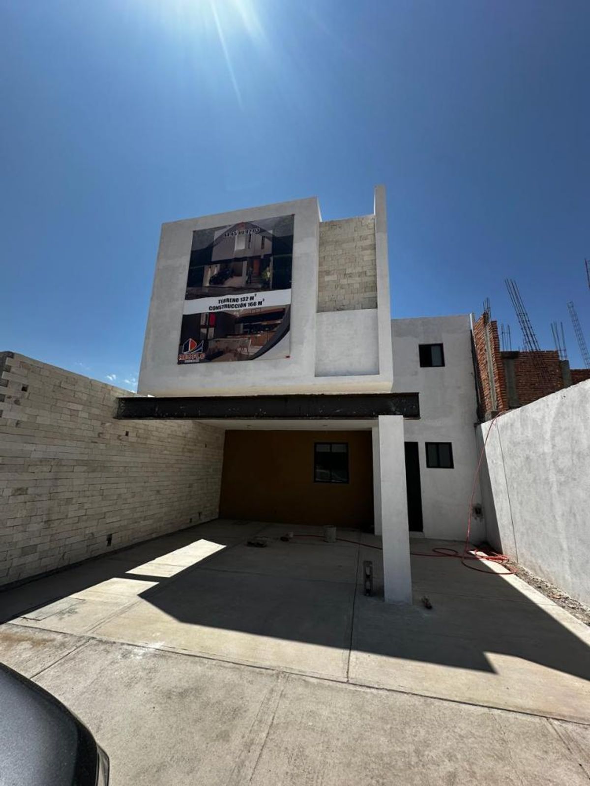 Fachada blanca de dos niveles con cochera, viga de acero y muro de piedra