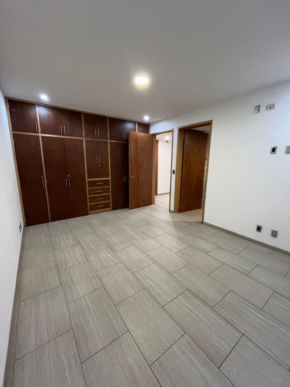 Habitación vacía con clóset de madera oscura empotrado, piso cerámico gris y paredes blancas