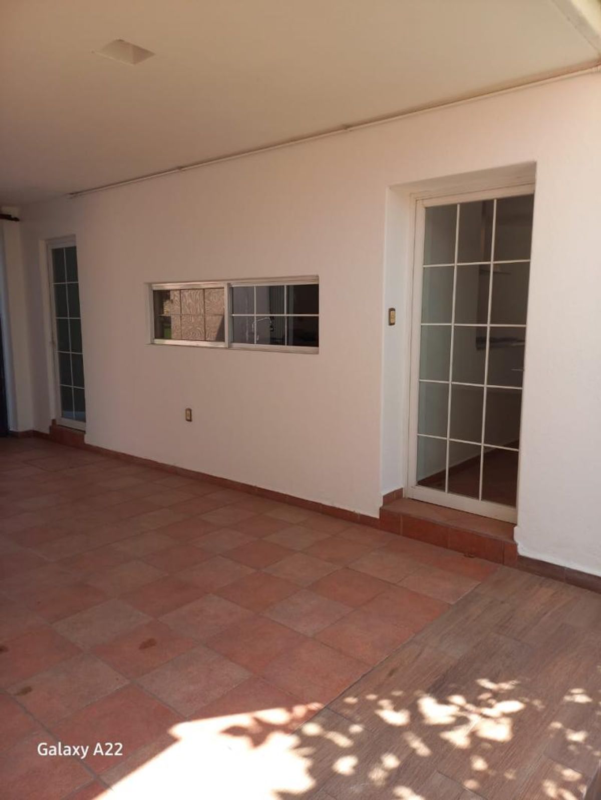 Patio techado con piso de terracota, paredes blancas, ventana horizontal y puerta de cristal