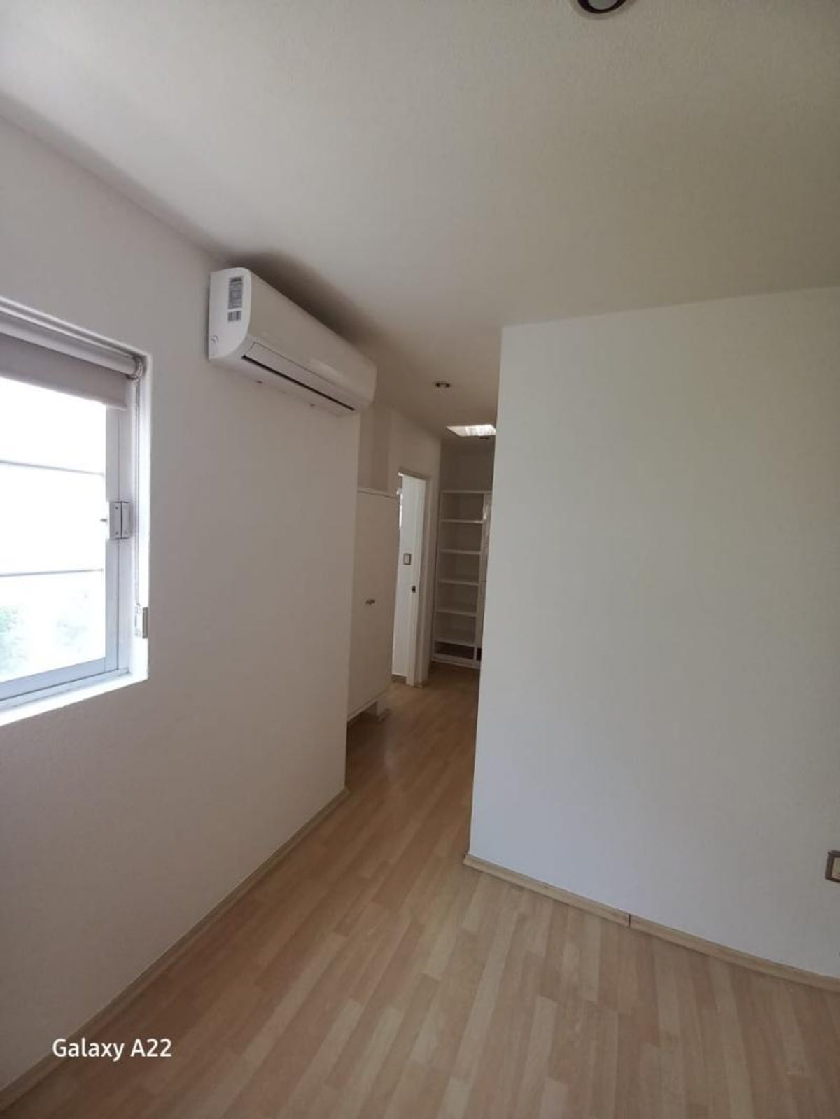 Habitación con piso laminado claro, aire acondicionado minisplit en la pared y ventana