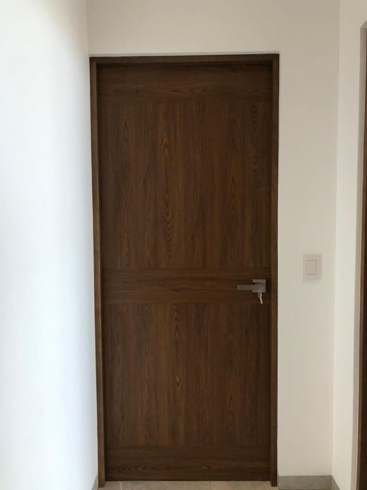 Puerta de madera oscura con manija metálica plateada y apagador en pared blanca