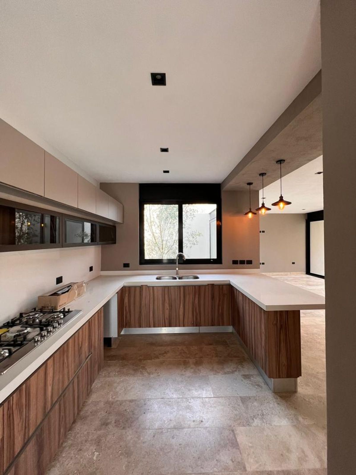 Cocina en U con barra, gabinetes de madera, cubiertas blancas, parrilla y lámparas colgantes