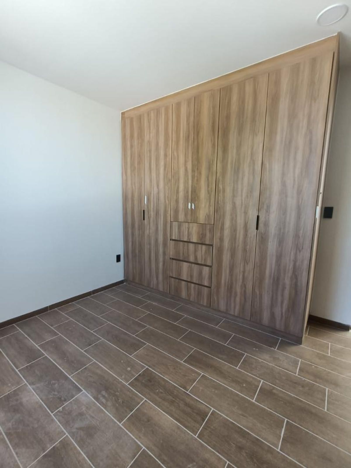 Habitación con amplio clóset empotrado de madera, paredes blancas y piso cerámico tipo madera