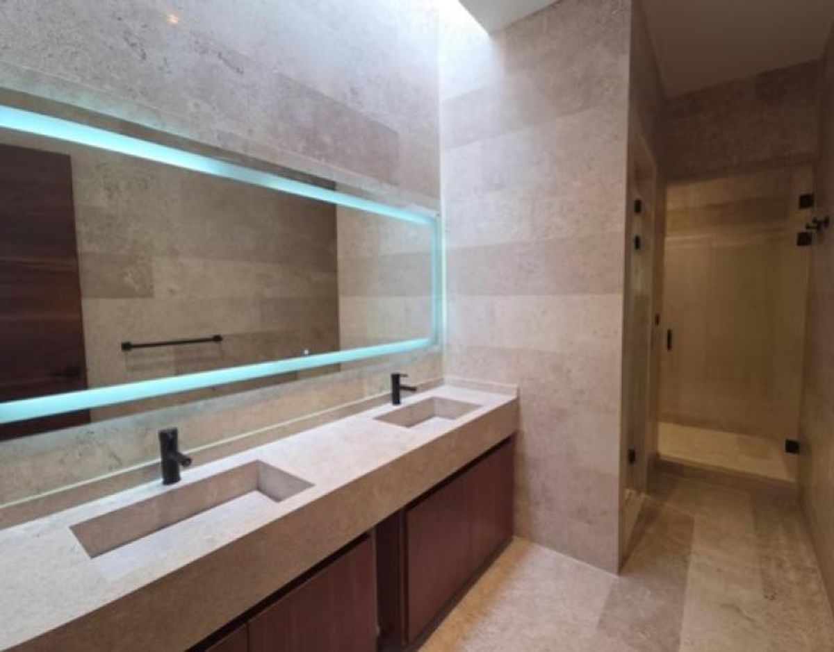 Baño con lavabo doble de piedra, grifería negra, espejo iluminado y muebles de madera