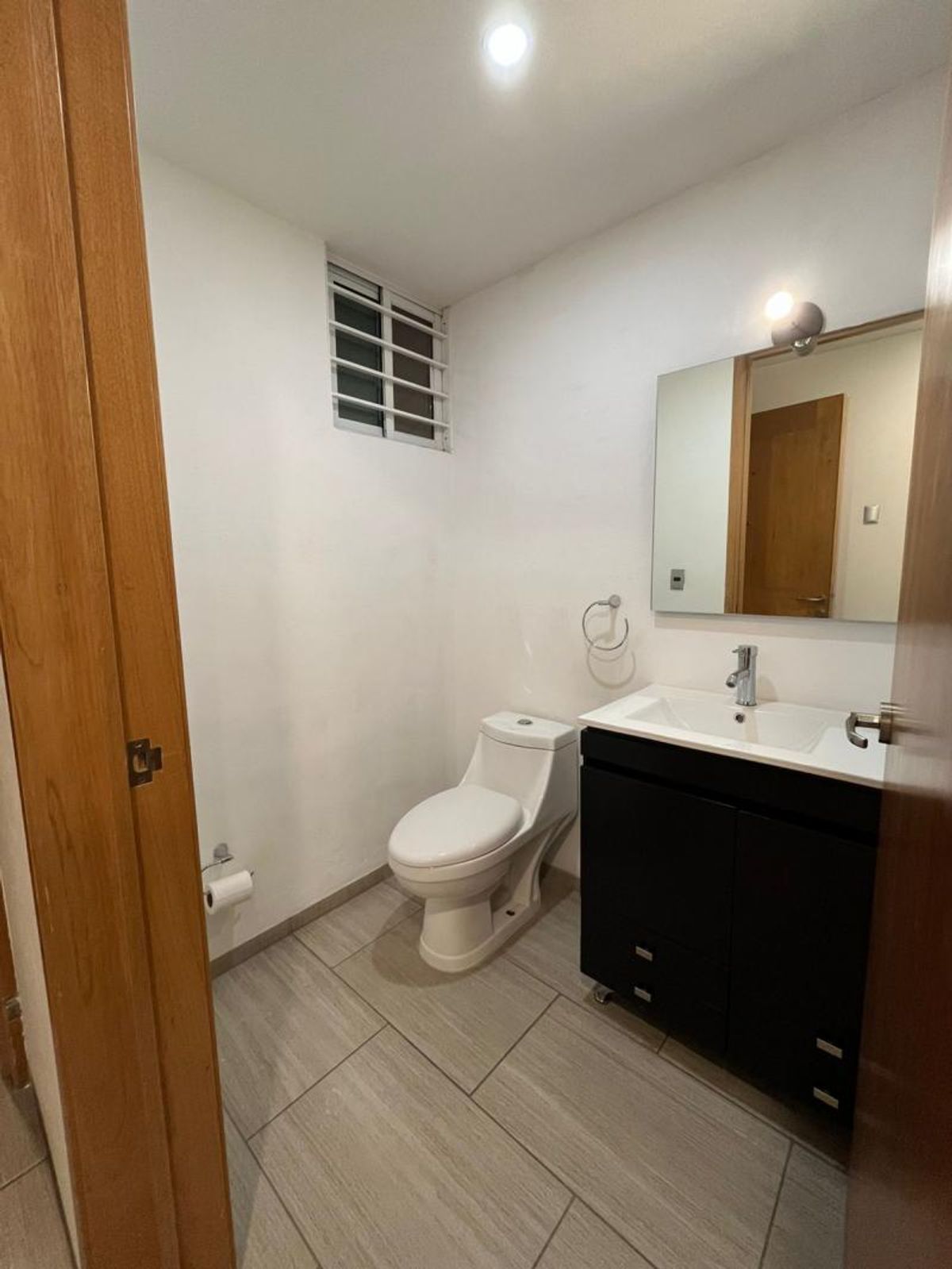 Baño con inodoro blanco, mueble de lavabo negro, espejo y piso de loseta gris