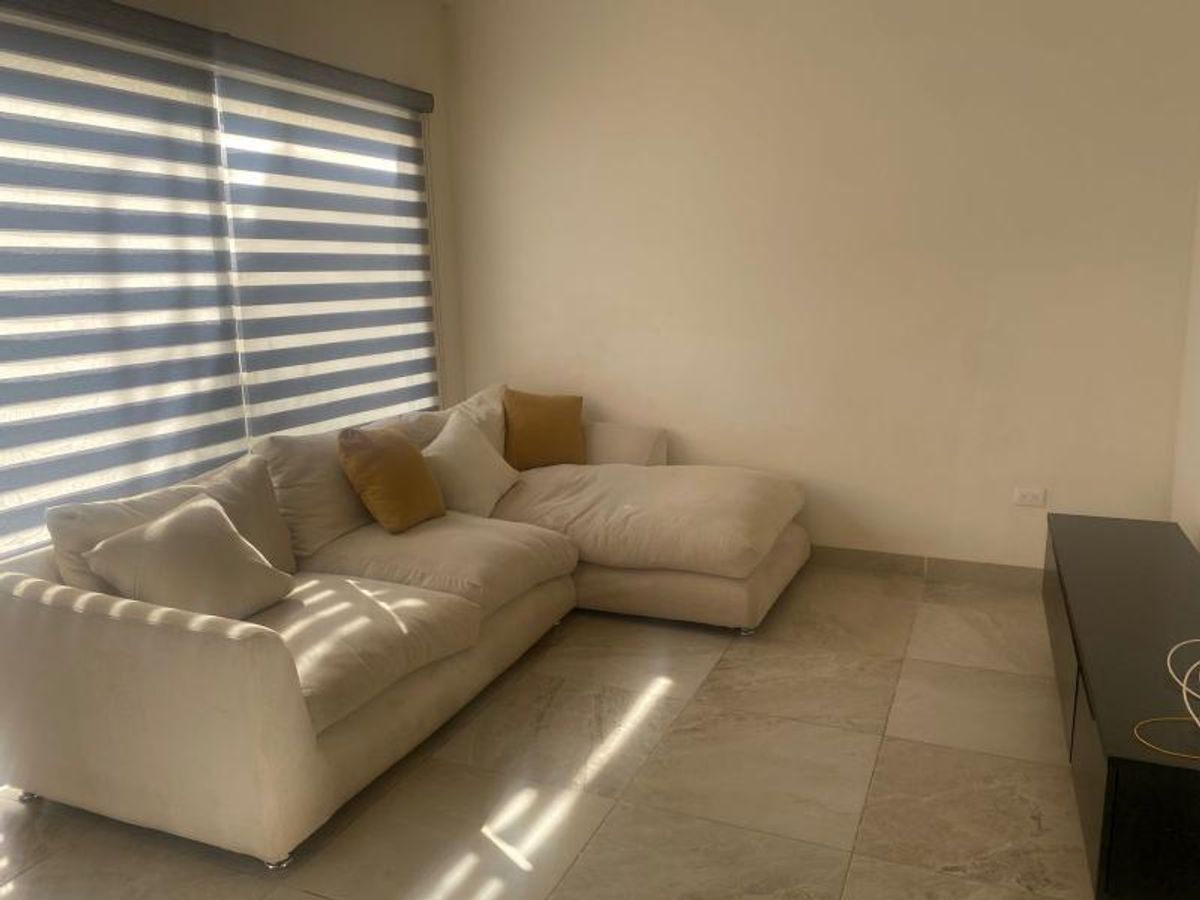 Sala con sofá modular beige, mueble de televisión oscuro y ventana con persiana cebra