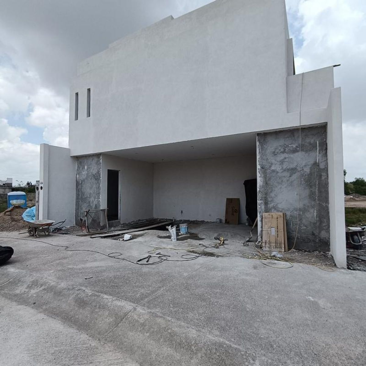 Fachada de casa moderna en construcción con muros blancos, cochera y acceso de concreto