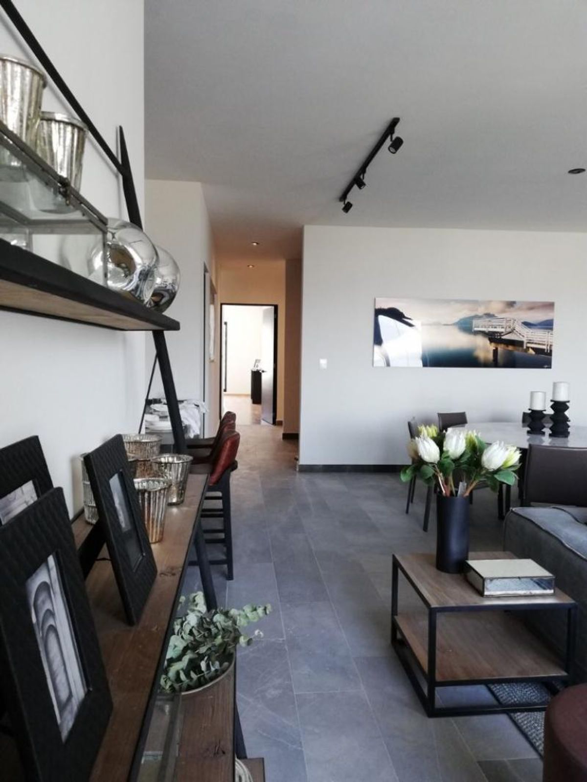 Sala con piso gris, consola de madera con decoraciones, cuadro panorámico y pasillo