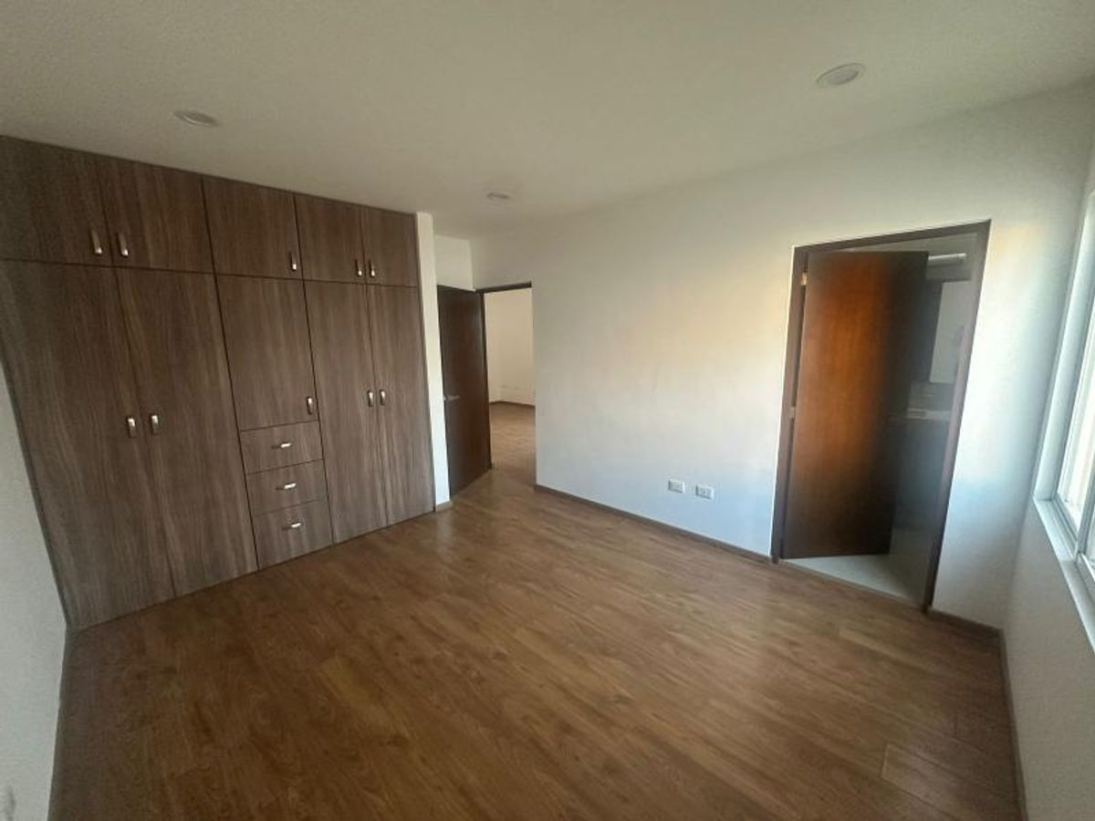Recámara con clóset de madera empotrado, piso de madera laminada y paredes blancas iluminadas