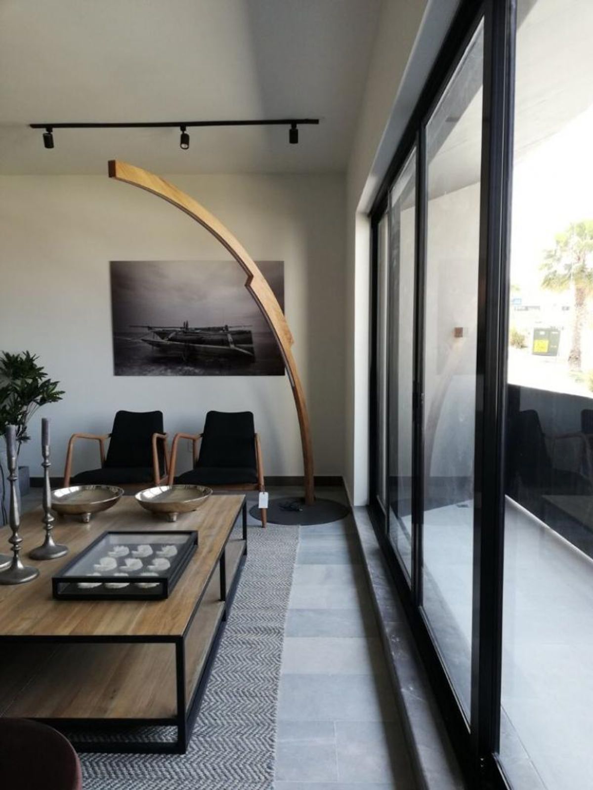 Sala con mesa de centro de madera, lámpara arqueada, sillones negros y ventanales corredizos