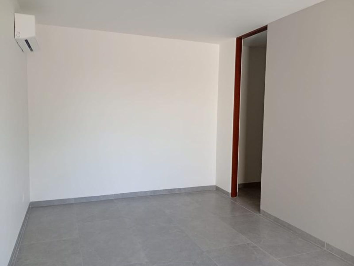 Habitación vacía con paredes blancas, piso cerámico gris, marco de madera y minisplit