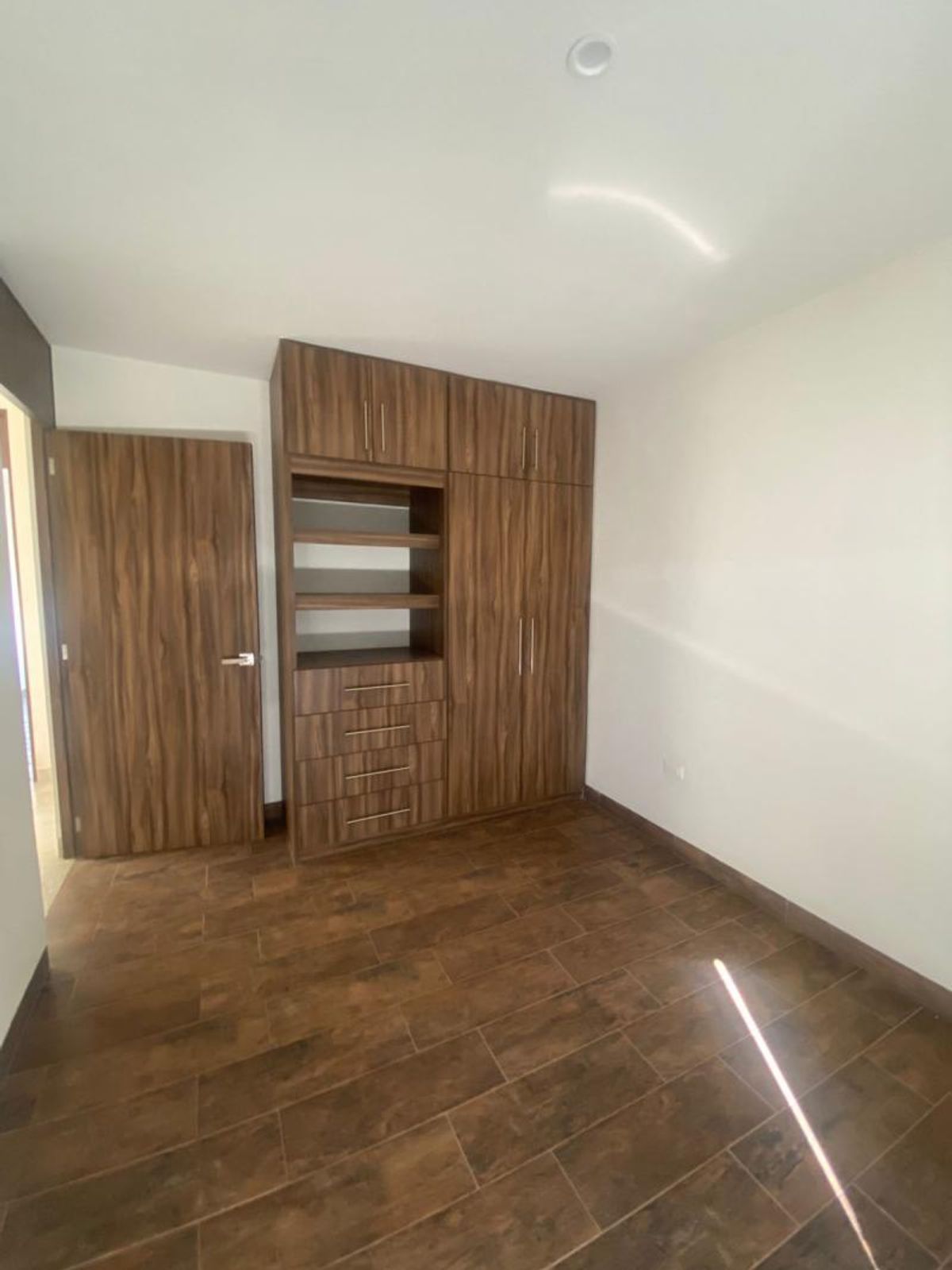 Recámara con piso tipo madera, puerta de madera y clóset con cajones y repisas