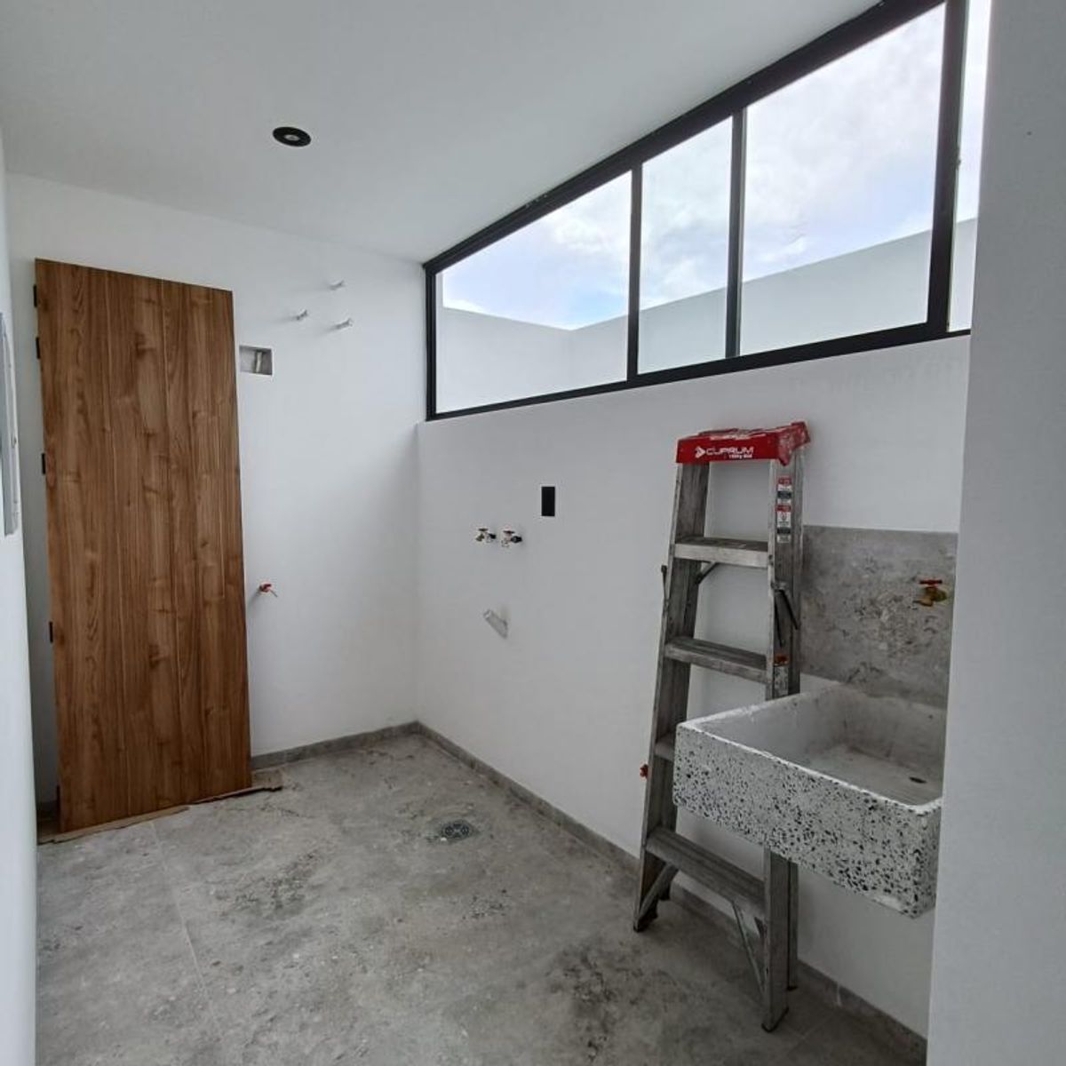 Cuarto de lavado con lavadero de terrazo, puerta de madera y ventana de marco negro