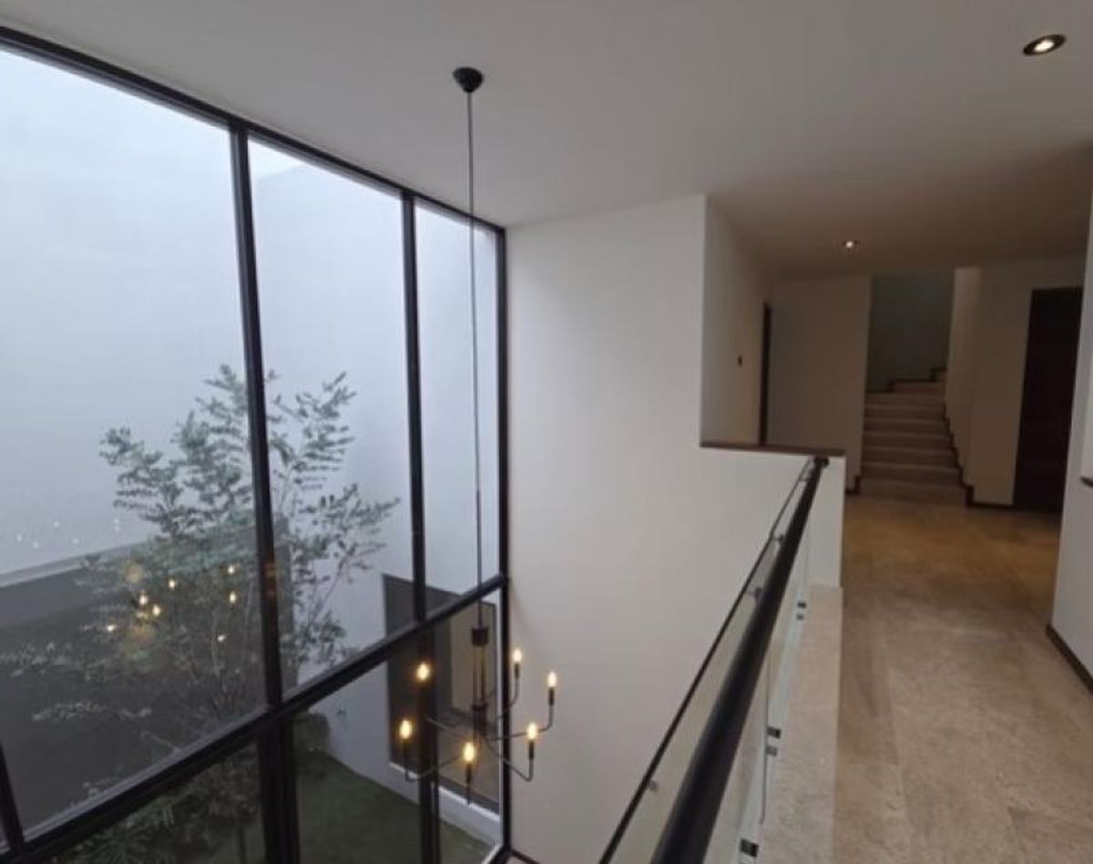 Pasillo con barandal de cristal, ventanal de doble altura y candelabro de metal colgante