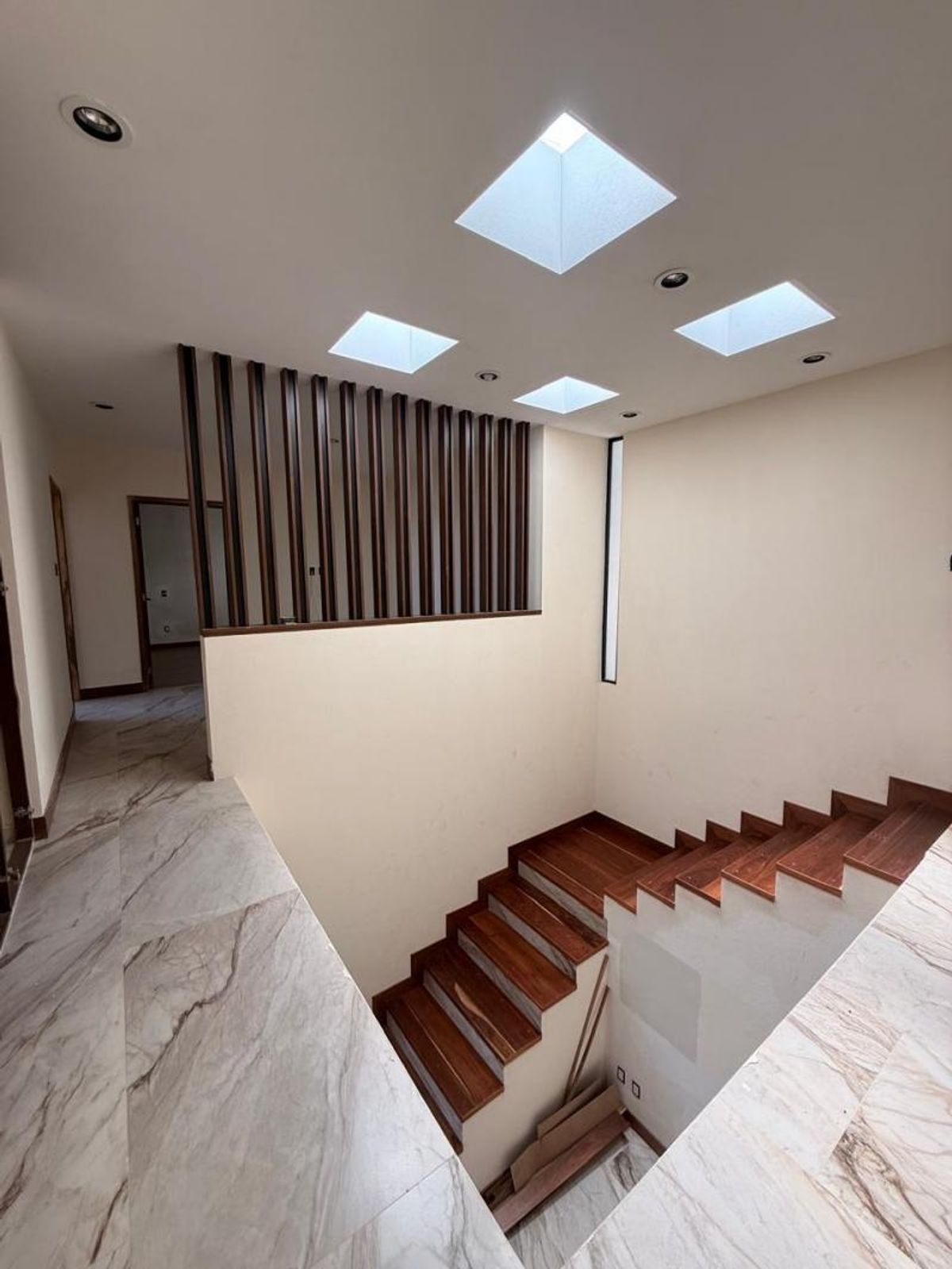 Escalera con escalones de madera, piso de cerámica veteada, celosía de madera y tragaluces
