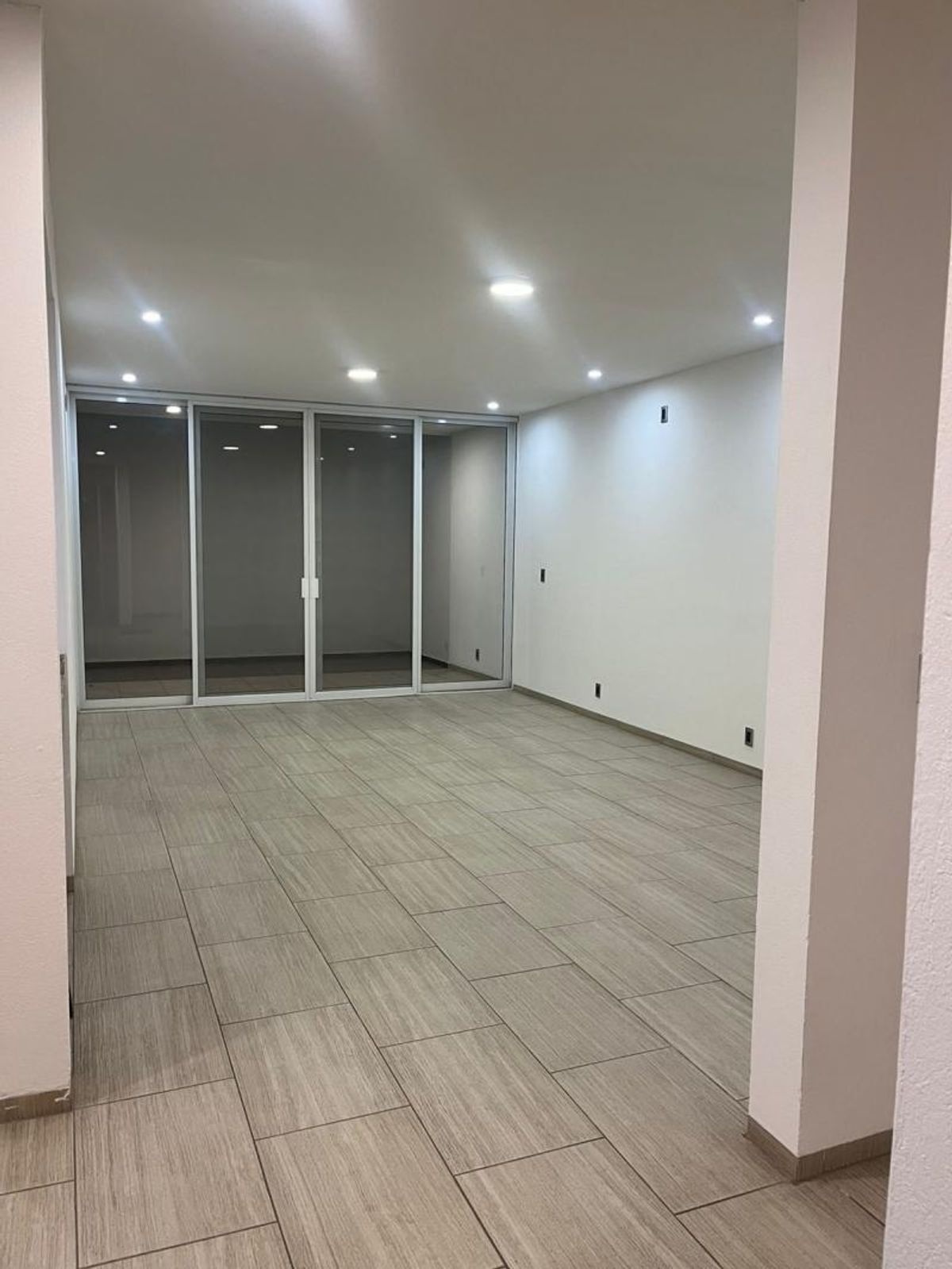 Habitación vacía con piso cerámico gris, iluminación empotrada y ventanales corredizos de cristal