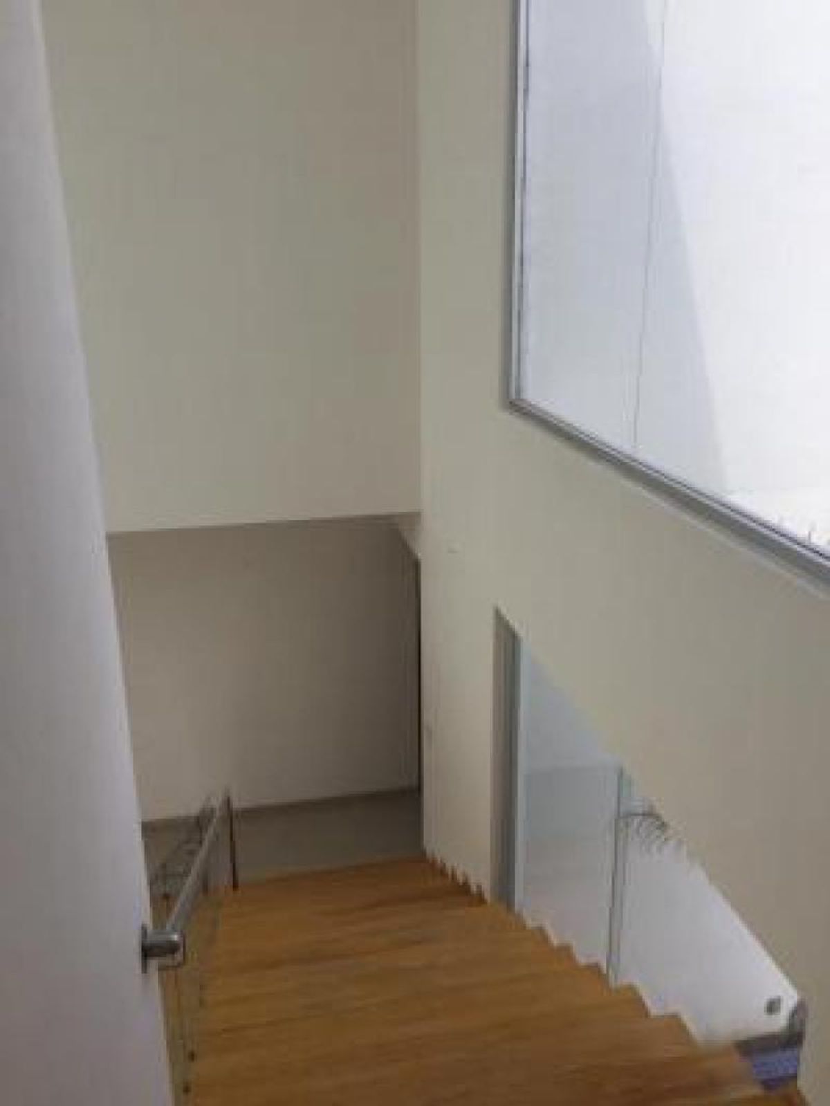 Escalera de madera con barandal de cristal, paredes blancas y amplio ventanal lateral
