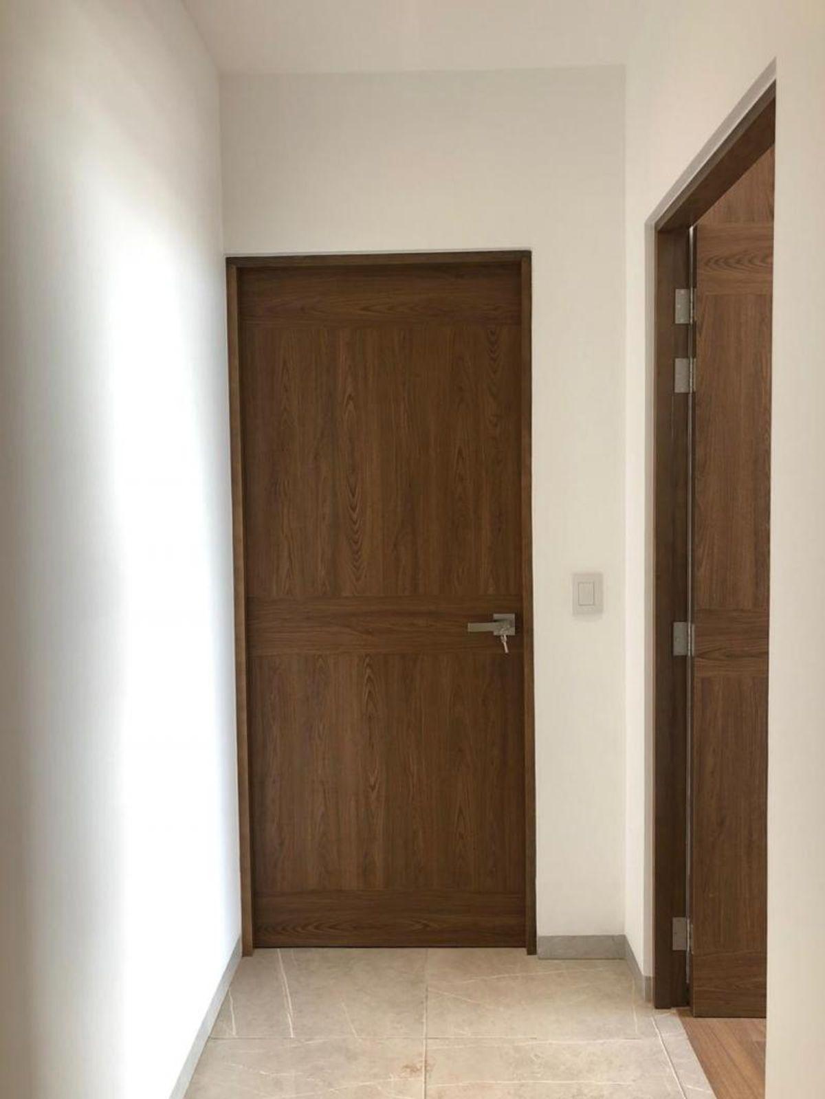 Pasillo interior con paredes blancas, piso de azulejo claro y puertas de madera marrón