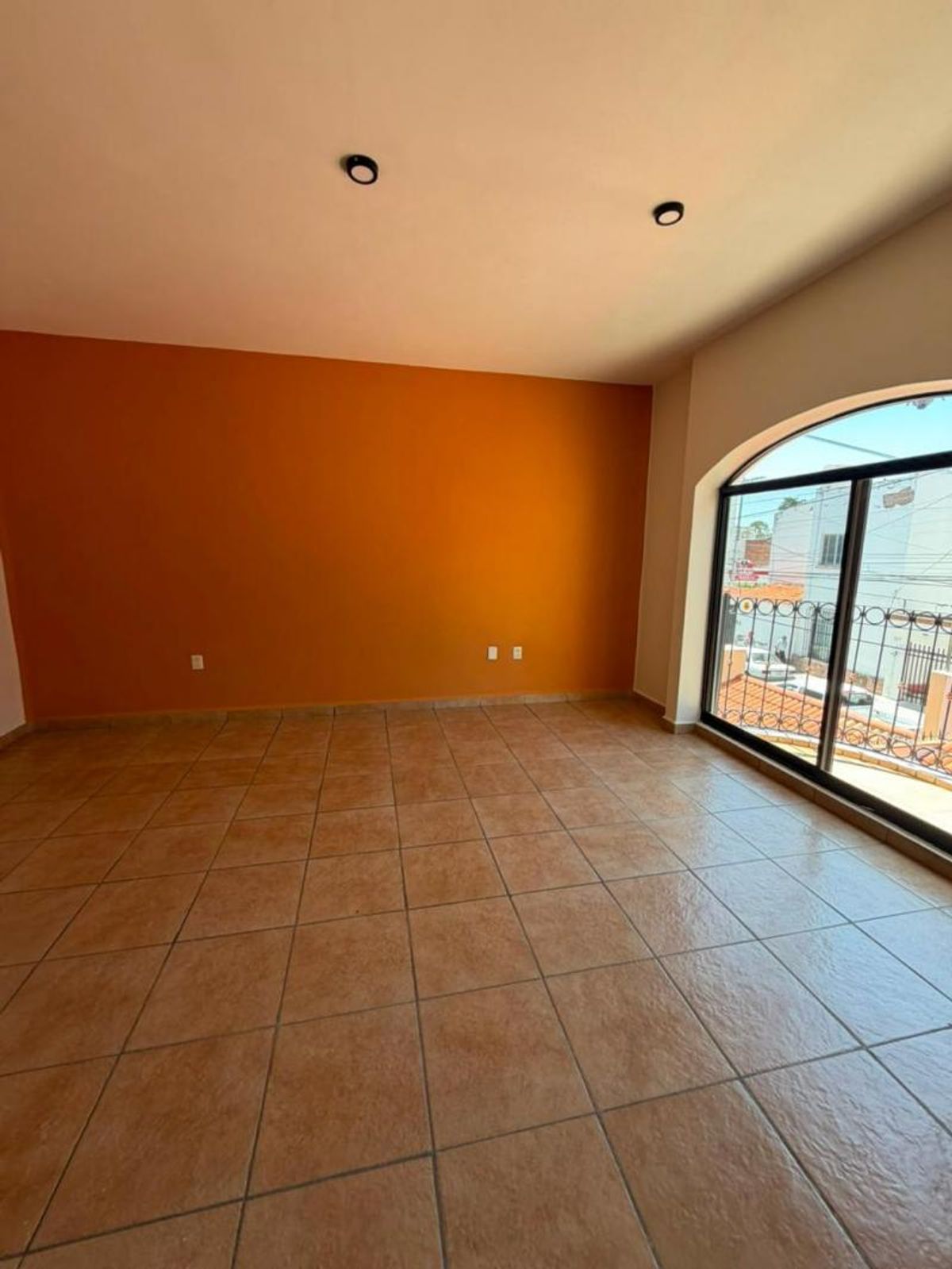 Espacio interior vacío con pared naranja, piso de cerámica y ventana arqueada