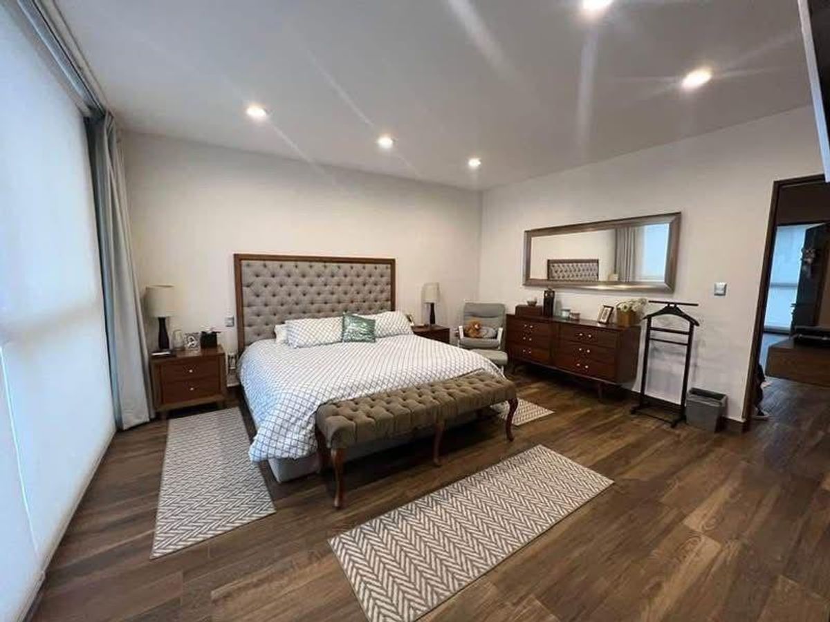 Recámara con cama de cabecera capitonada, banca a los pies, cómoda y piso de madera