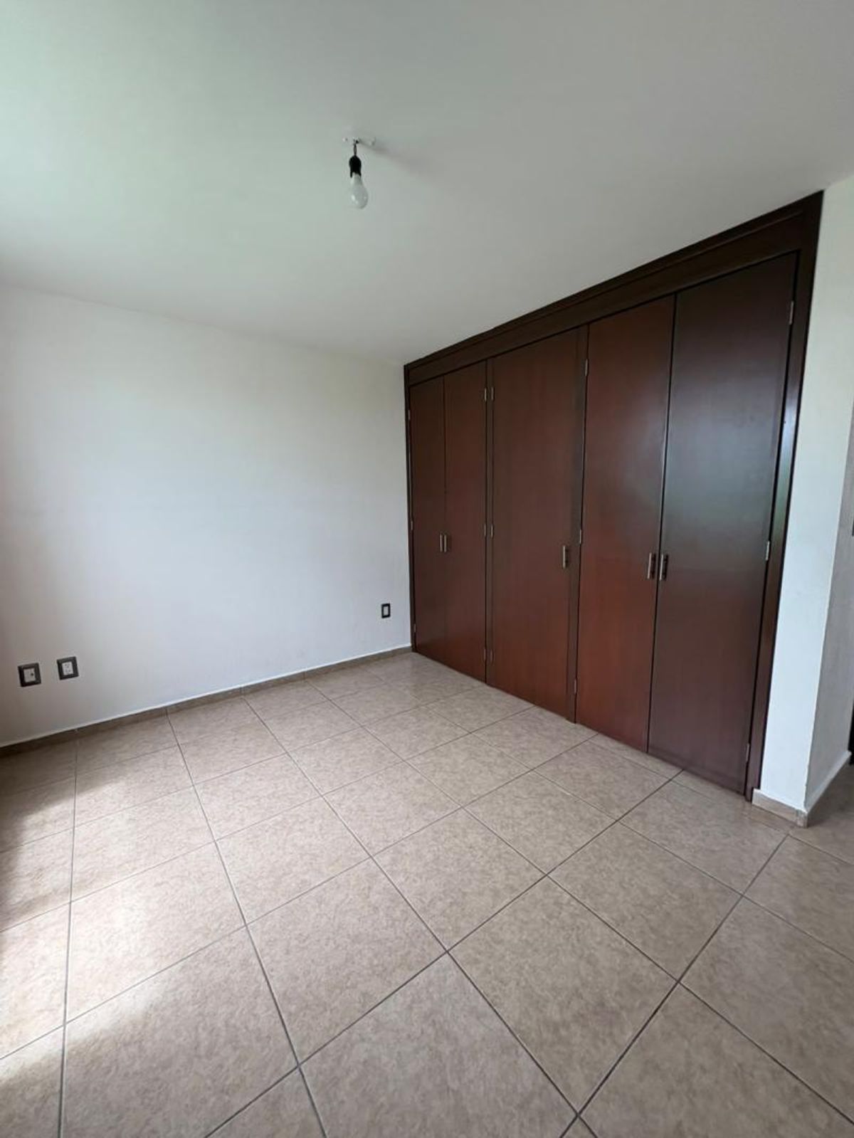 Habitación vacía con piso de cerámica beige, paredes blancas y clóset de madera oscura