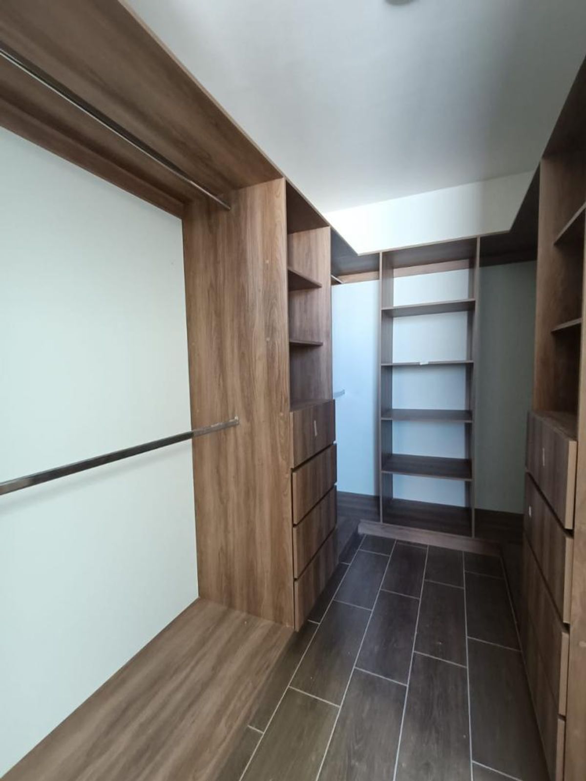 Vestidor de madera con repisas, cajoneras, barras metálicas y piso de cerámica oscura