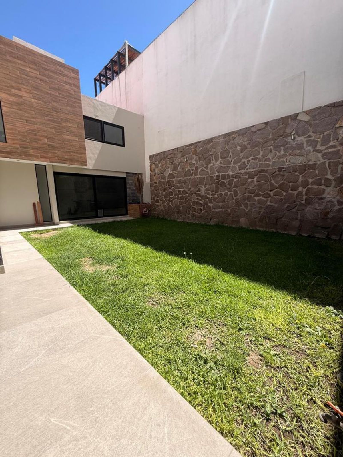 Jardín trasero con césped, muro perimetral de piedra y terraza de piso claro