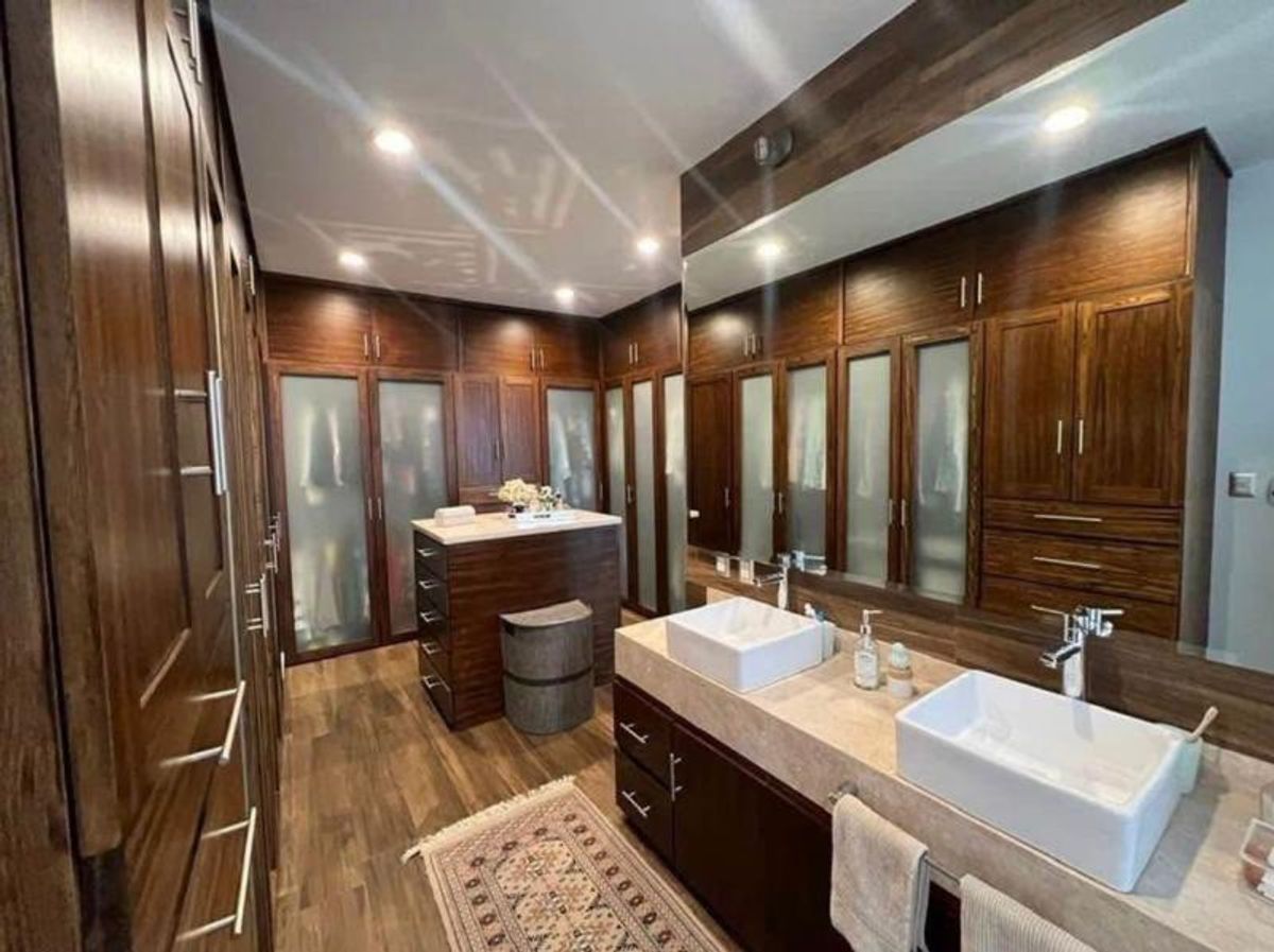 Vestidor con closets de madera oscura, cristal opaco, isla central y doble lavabo blanco