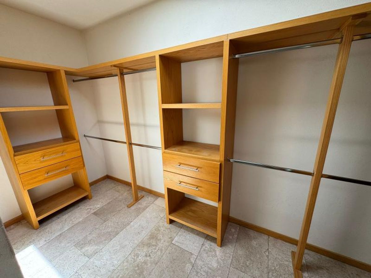 Vestidor de madera clara con repisas, cajones, barras para colgar ropa y piso claro