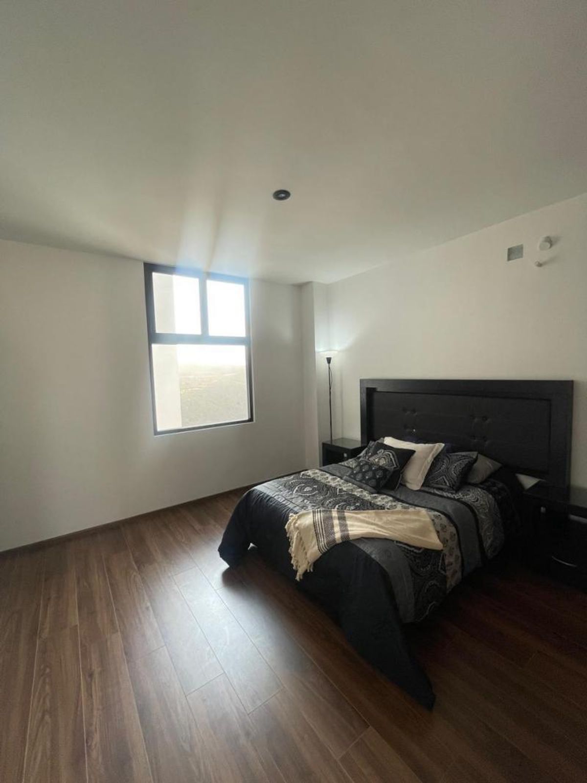 Recámara con piso de madera, ventana con luz natural y cama con cabecera negra