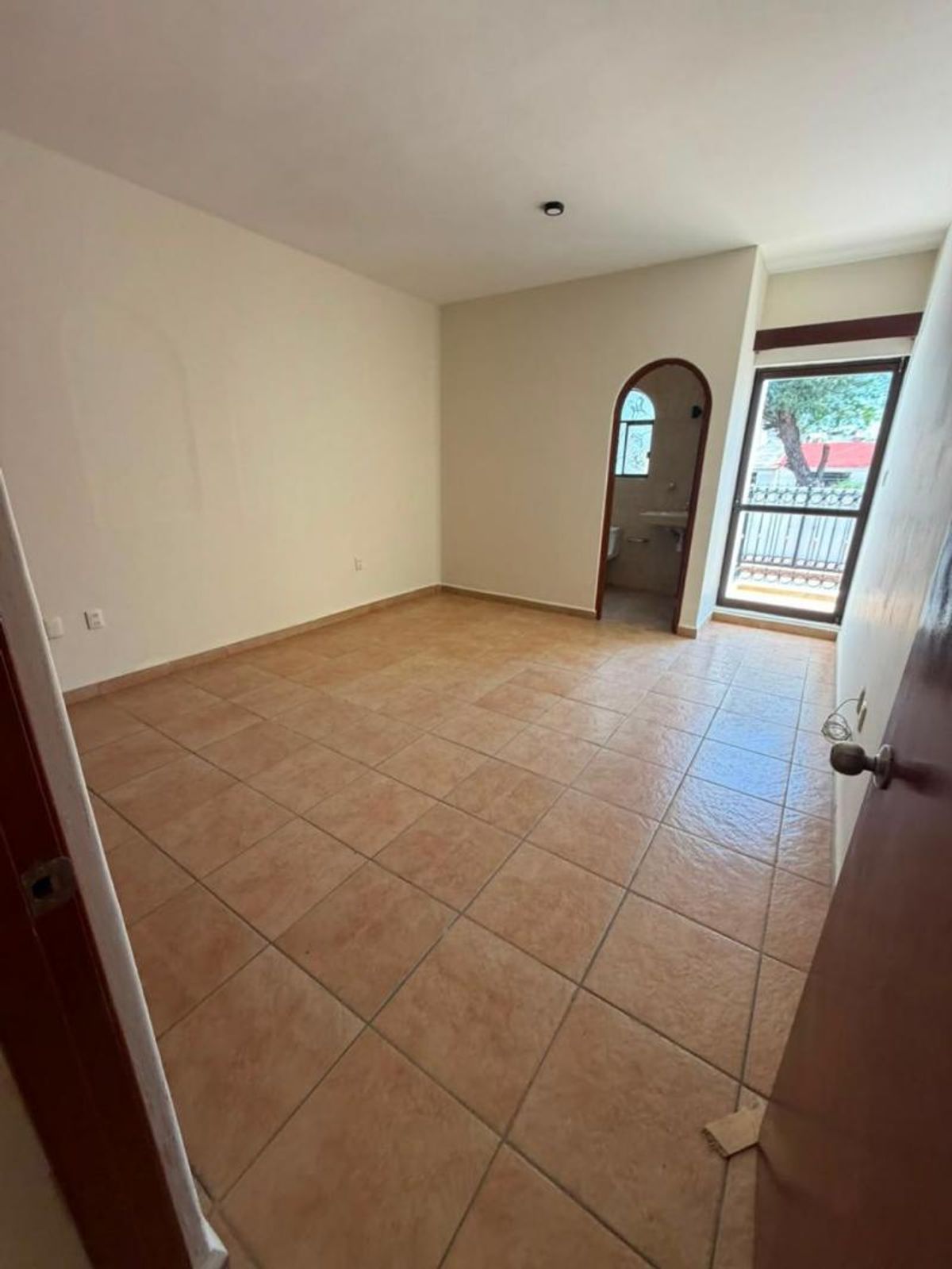 Habitación vacía con piso de cerámica beige, arco de acceso al baño y ventanal