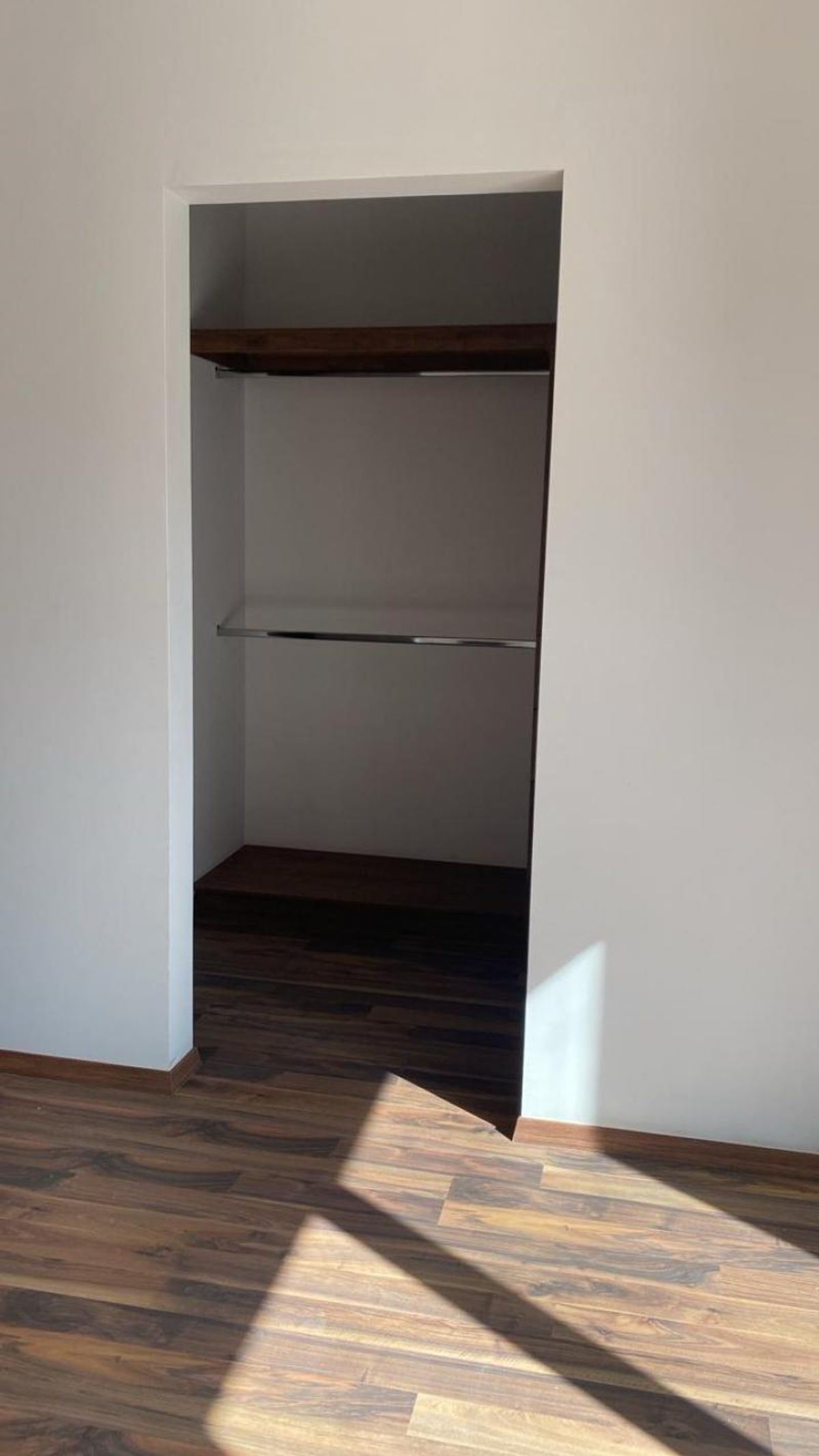 Closet abierto con repisas de madera oscura, tubos para colgar y piso laminado