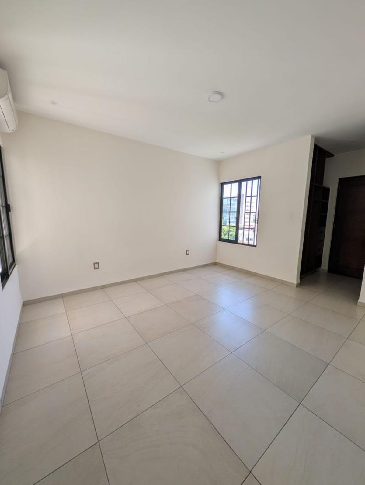 Habitación vacía con piso de loseta beige, paredes blancas y ventanas con marcos oscuros