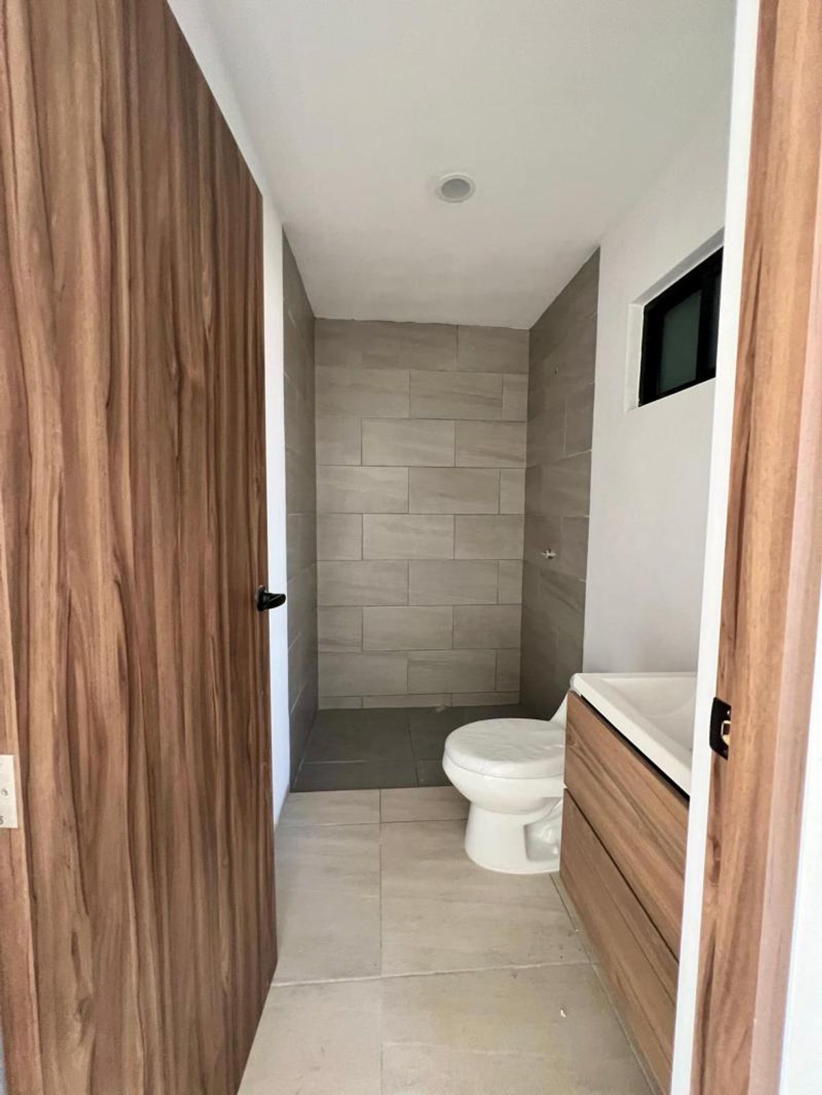 Baño con inodoro blanco, mueble de madera con lavabo y paredes revestidas de azulejos