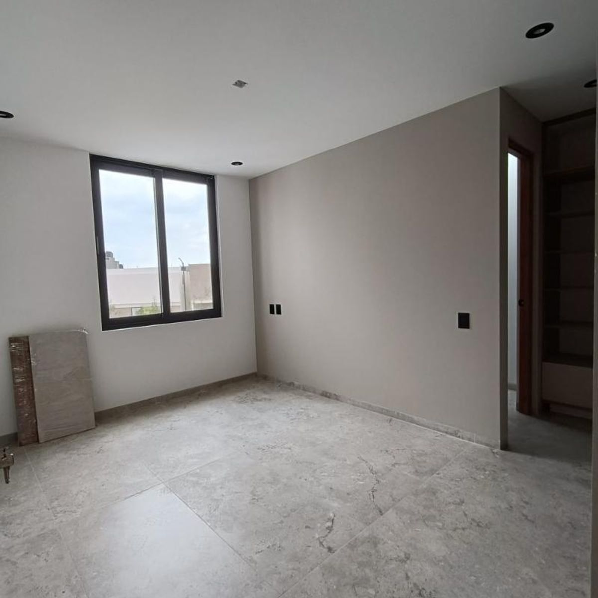 Habitación vacía con piso de porcelanato gris, pared taupe y ventana de marco negro
