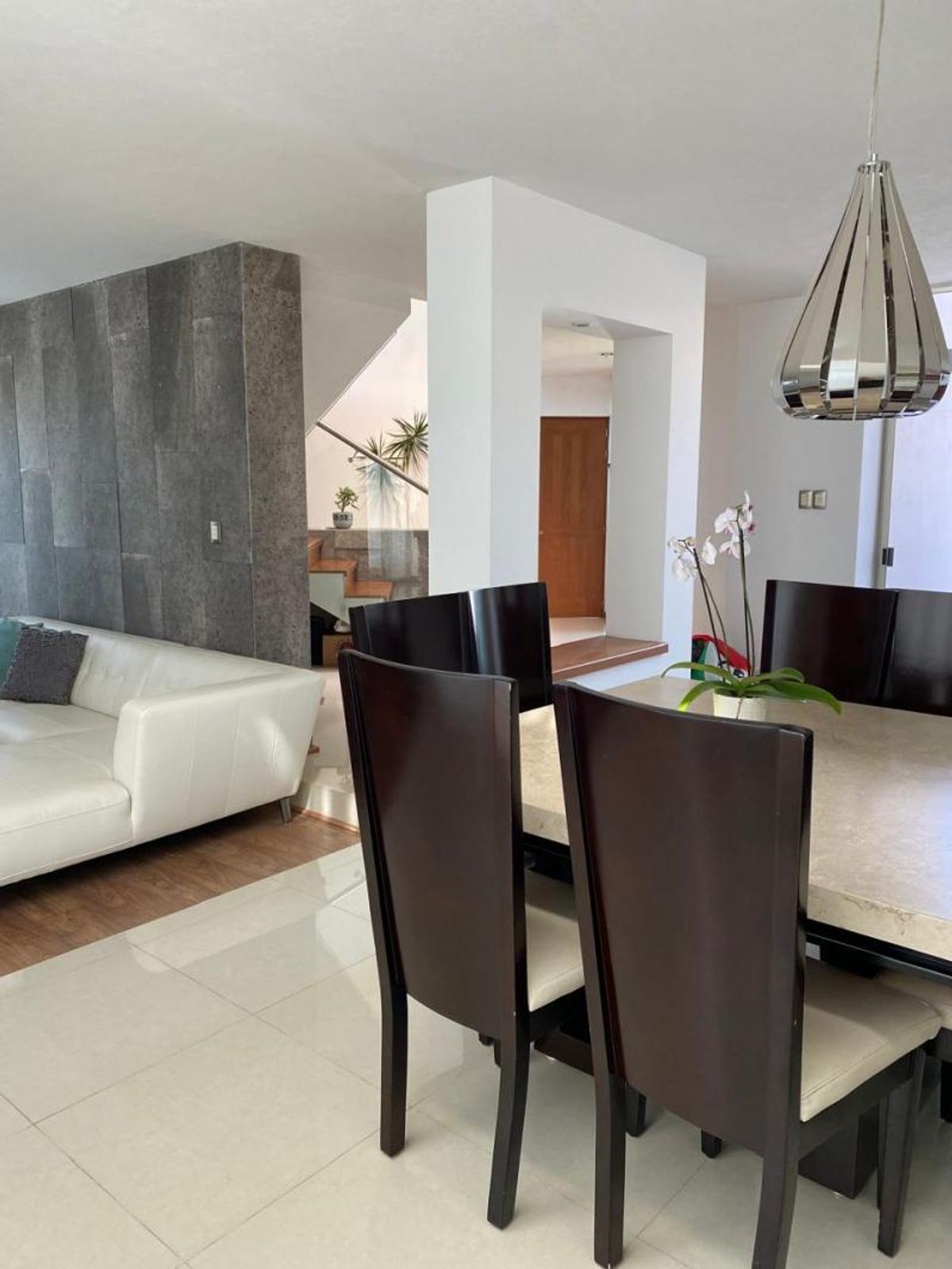 Comedor con sillas de madera oscura, mesa clara y sala contigua con sofá blanco