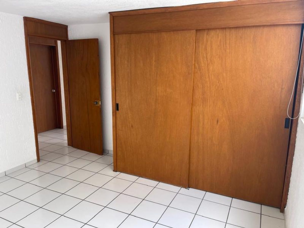 Habitación con closet de madera, puertas corredizas, paredes blancas y piso de azulejo blanco
