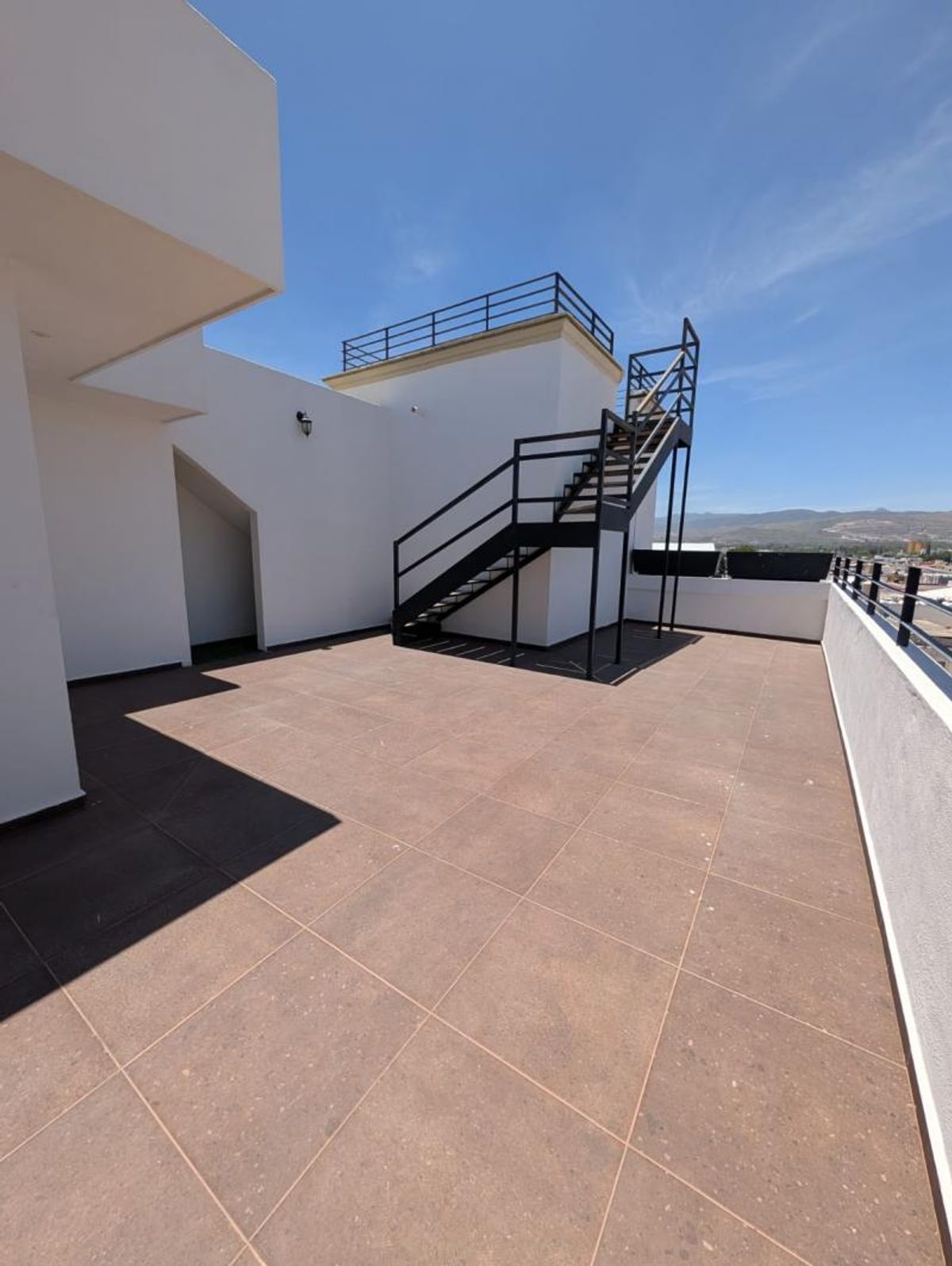 Terraza al aire libre con piso de loseta, paredes blancas y escalera metálica negra