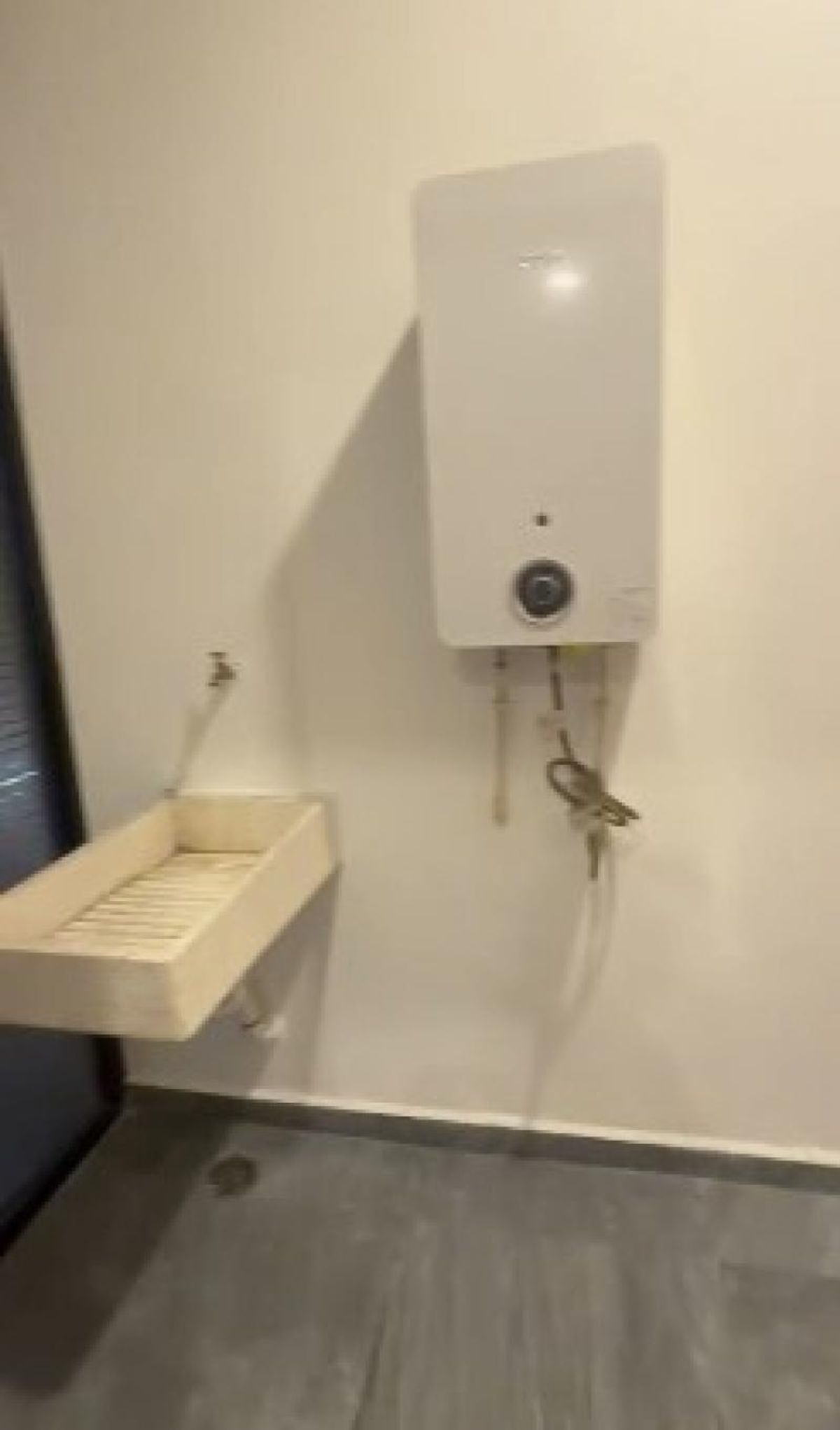 Área de lavado con calentador de agua mural, lavadero con grifo y piso gris