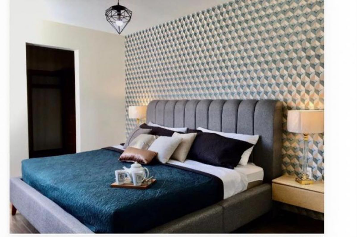 Recámara con cama tapizada gris, edredón azul y pared con papel tapiz geométrico