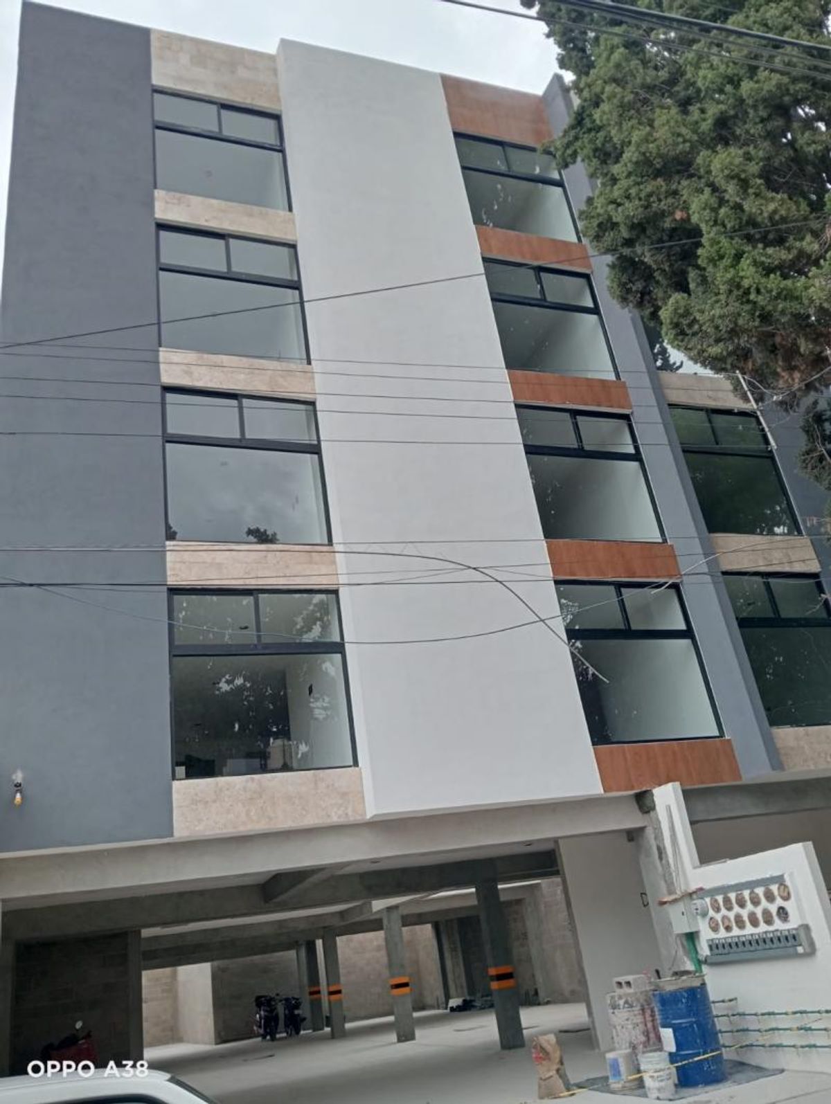 Fachada de edificio residencial moderno con amplios ventanales, detalles en gris y estacionamiento techado