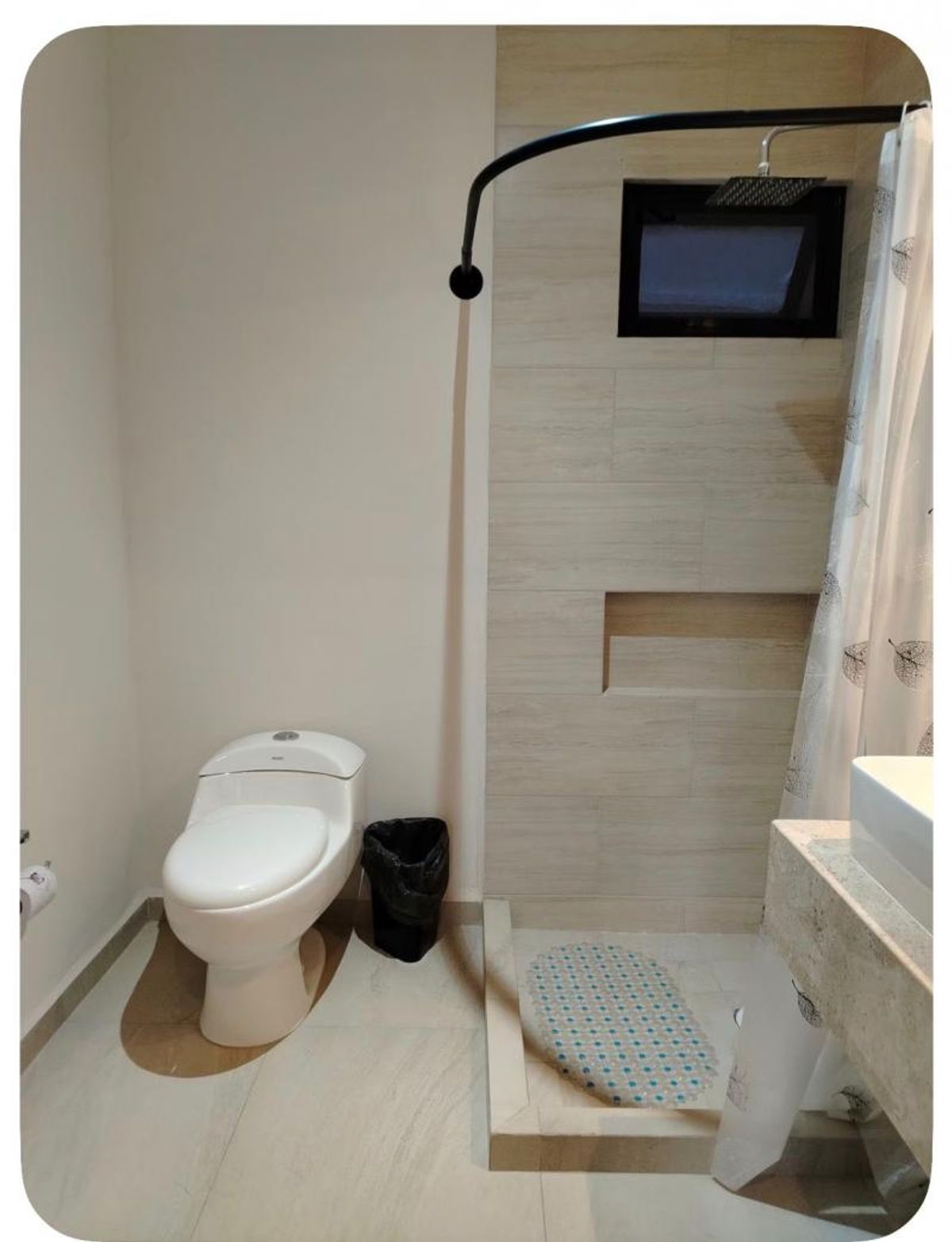 Baño con inodoro blanco, área de regadera revestida de loseta beige, nicho y cortina