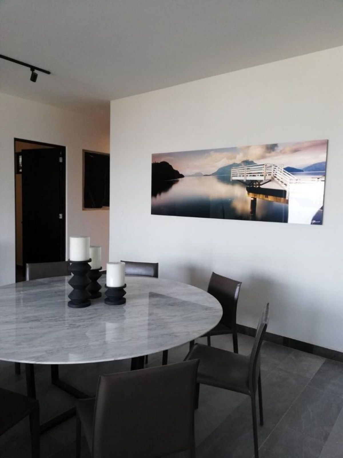 Comedor con mesa redonda de mármol gris, sillas oscuras y un cuadro panorámico