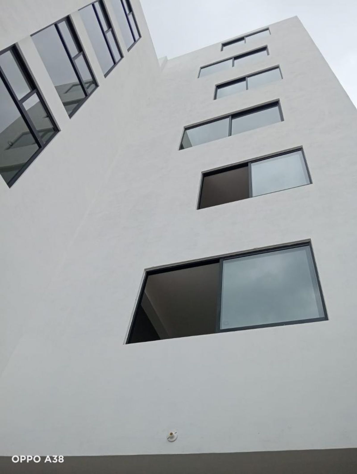 Fachada blanca de edificio con ventanas rectangulares y marcos oscuros vista desde abajo